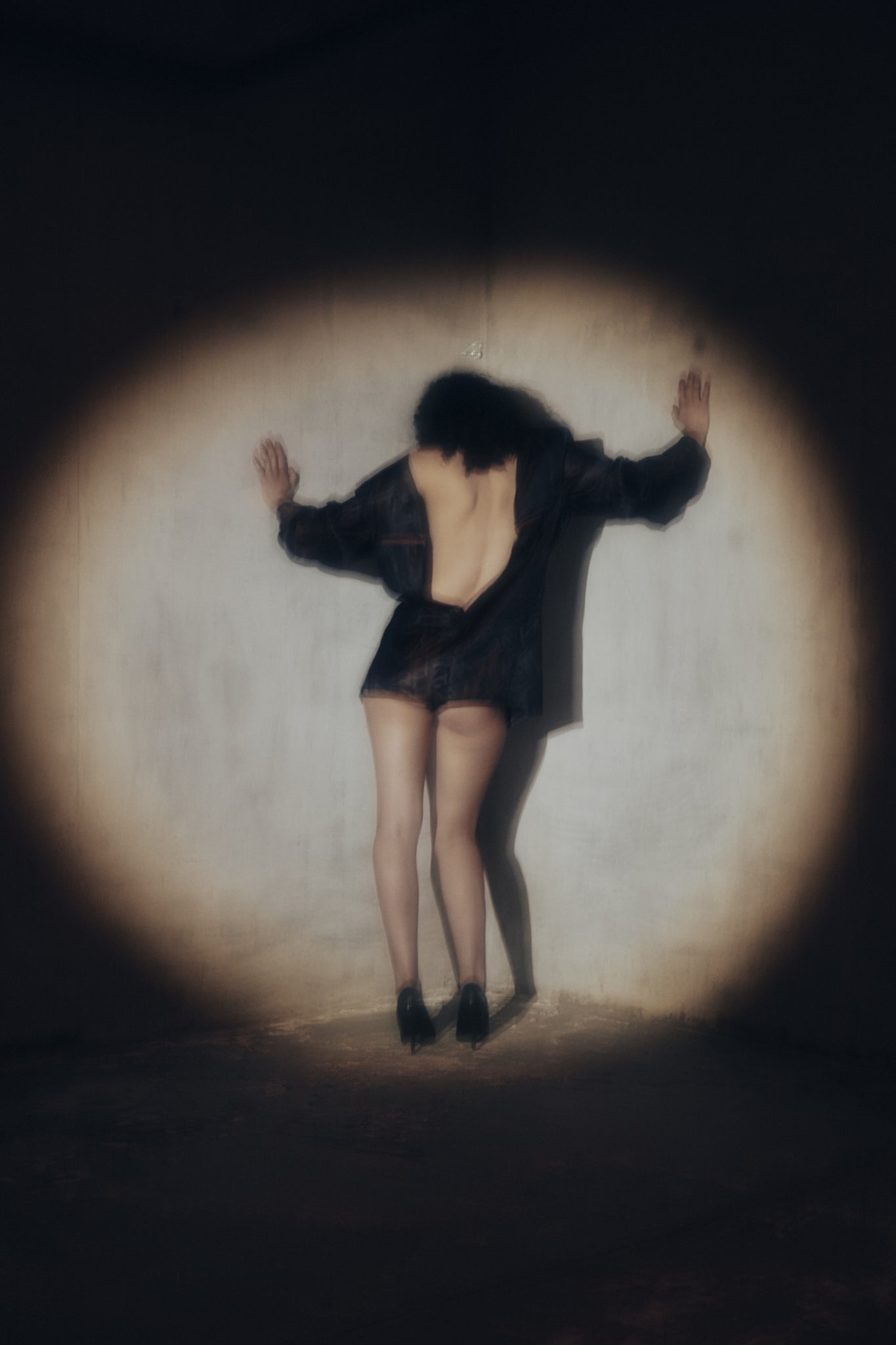 Taus Autumn Winter 2026, back view of a model in a short black open-back dress in a circle of spotlight