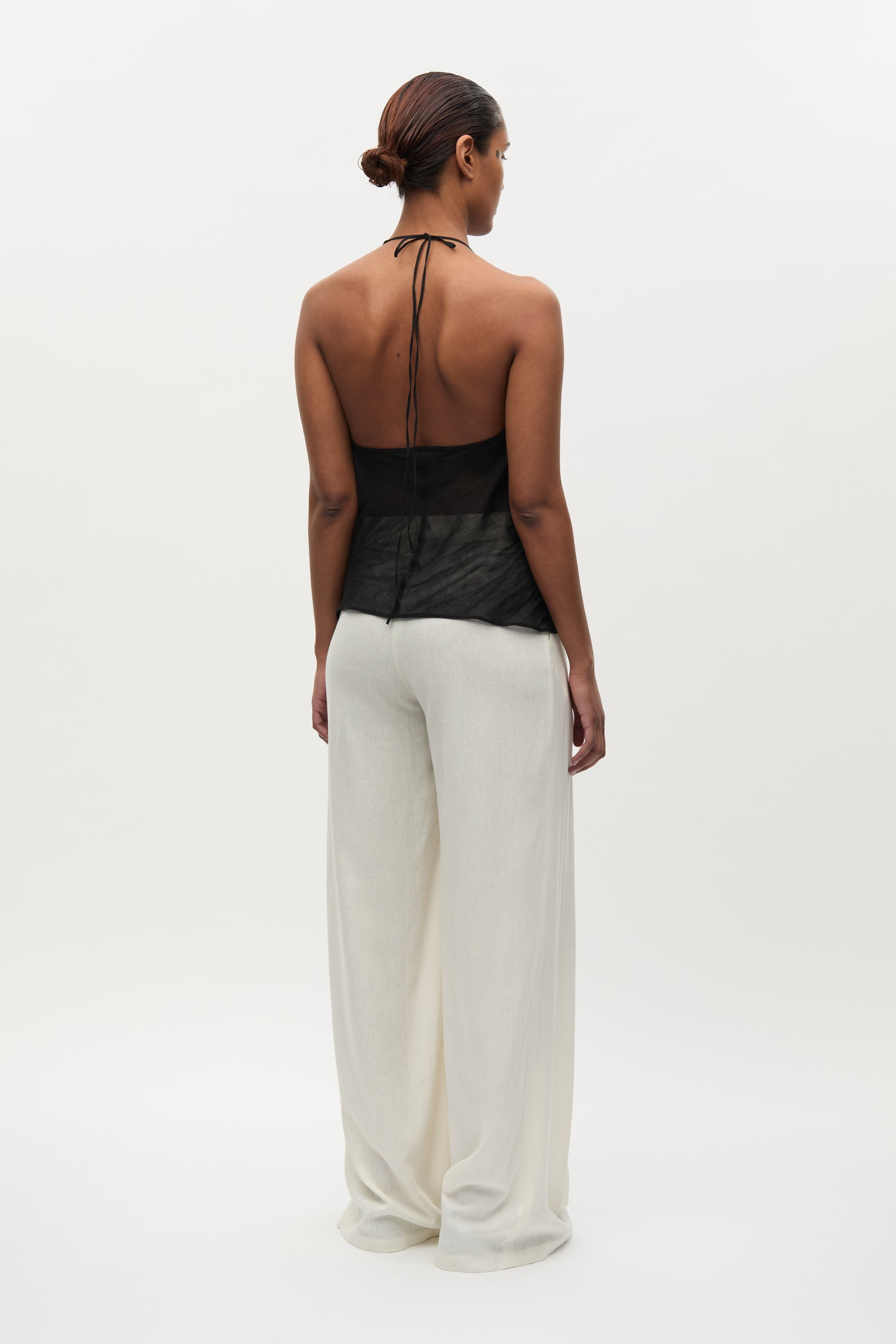 Woman wearing a black halter top and white pants on a white background
