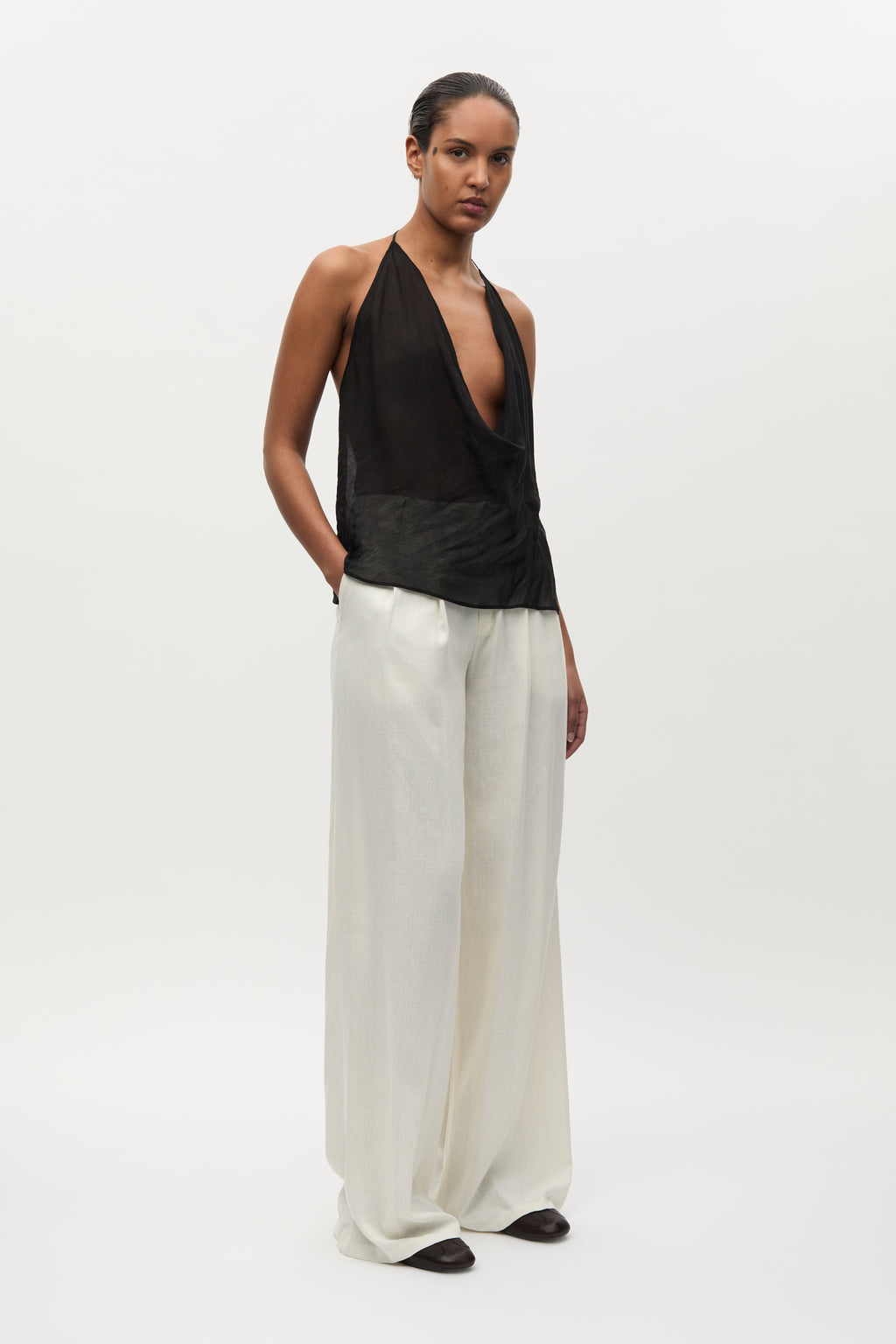 Woman wearing a black halter top and white pants on a white background