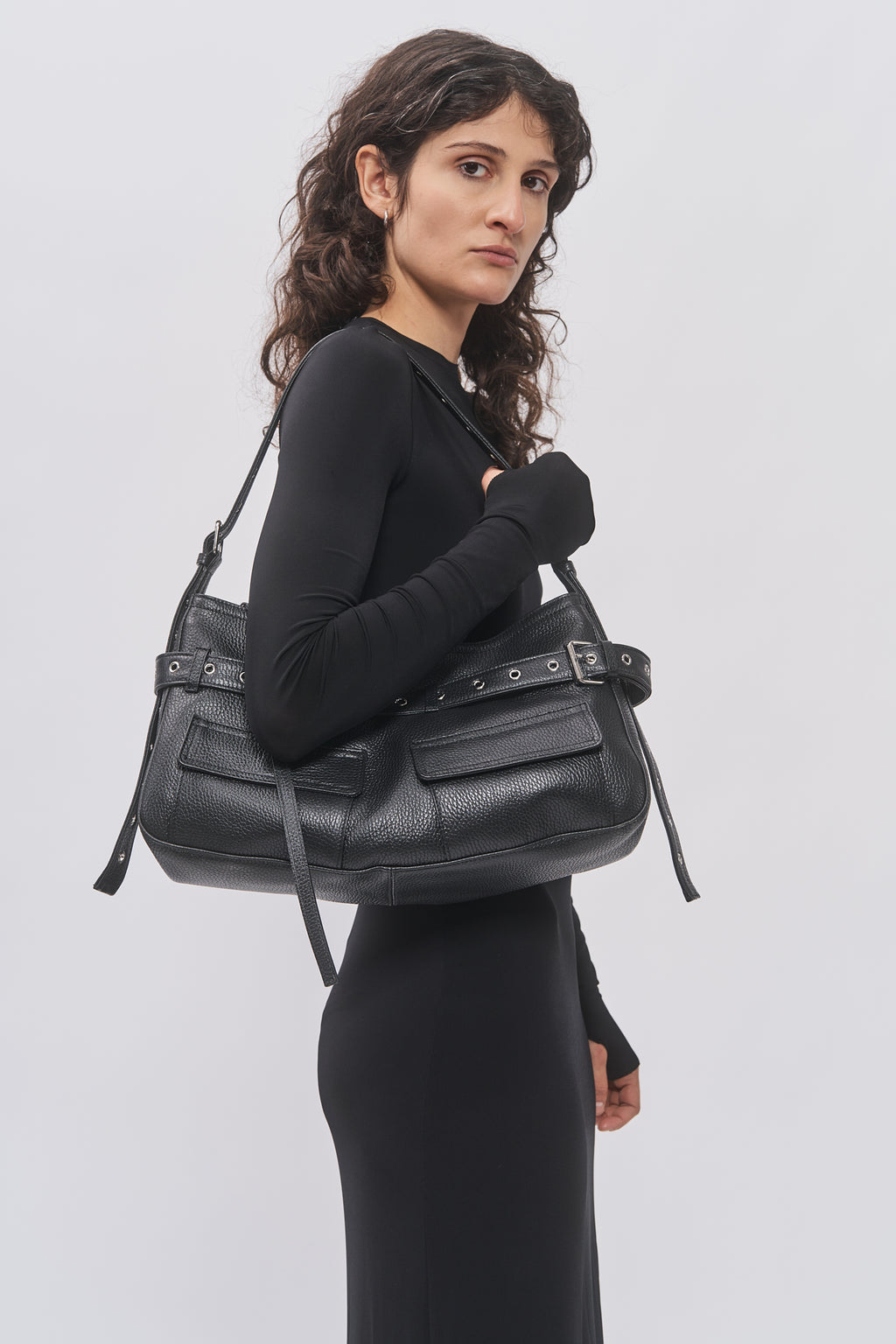 Taus Juho Bag Small in black leather with belt and eyelet details, worn on the shoulder with a black dress