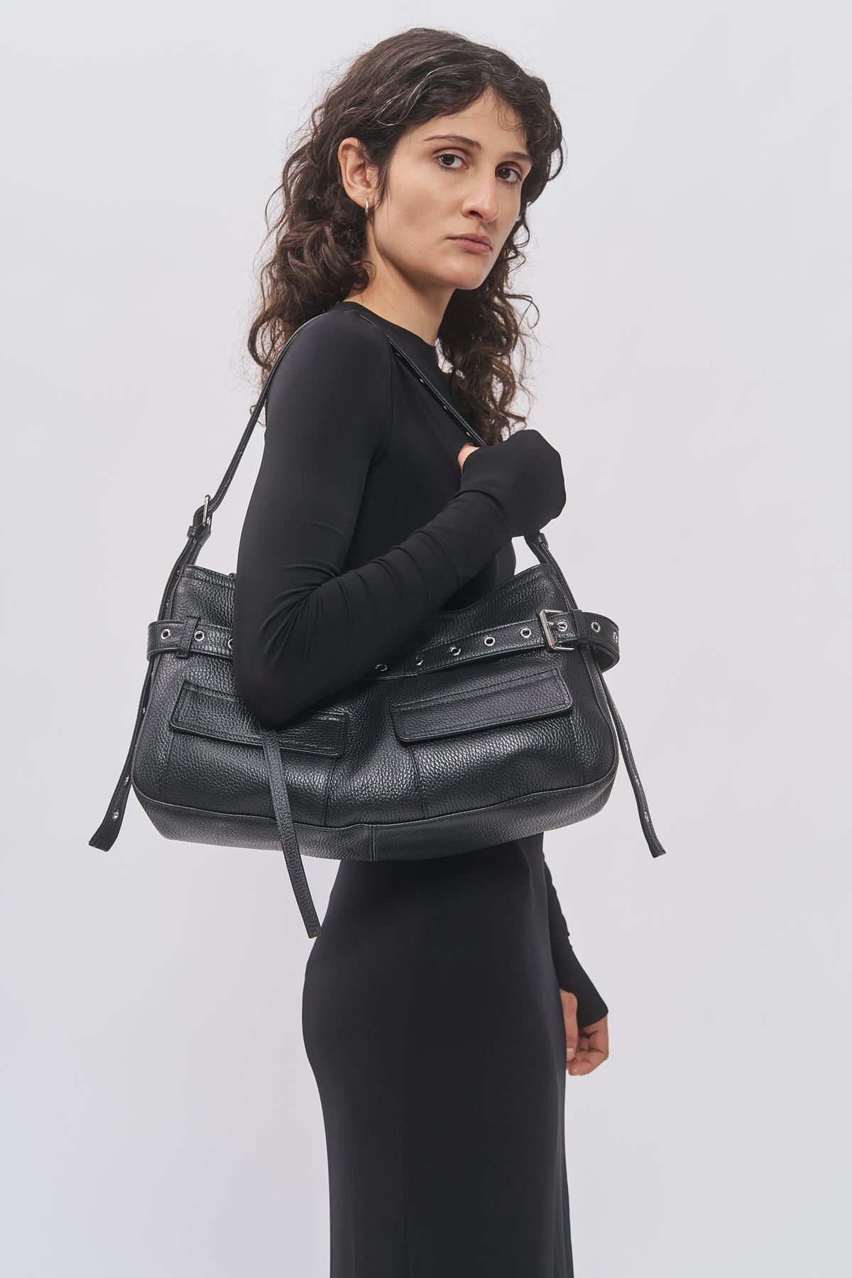 Taus Juho Bag Small in black leather with belt and eyelet details, worn on the shoulder with a black dress