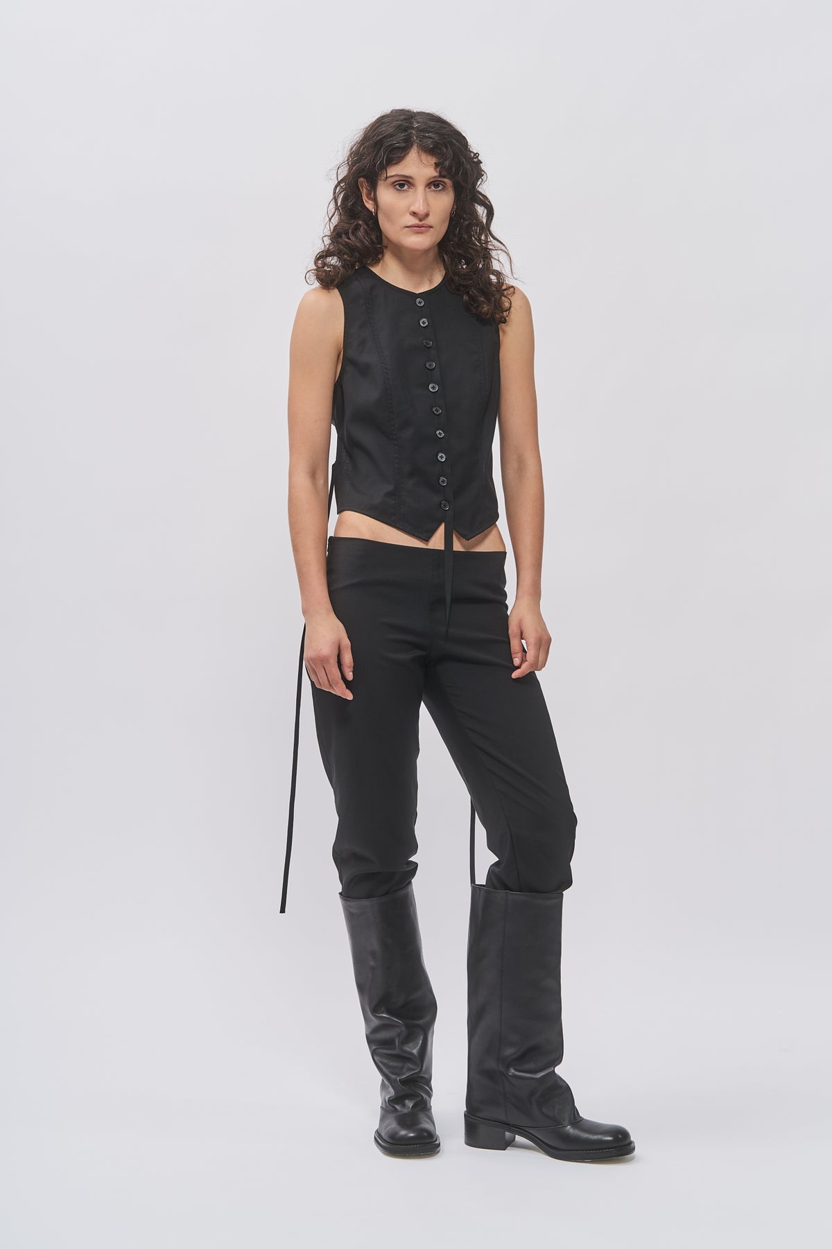 Taus Open-Back Waistcoat in black, cropped button-front vest with ties, worn with black low-rise trousers