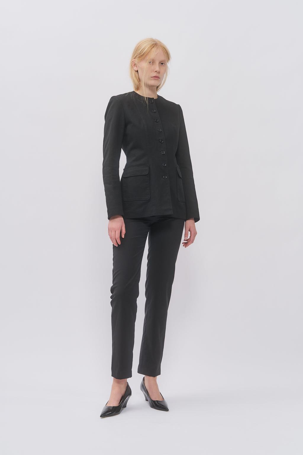 Taus Tailored Jacket in black, collarless fitted jacket with flap pockets, worn with black slim trousers