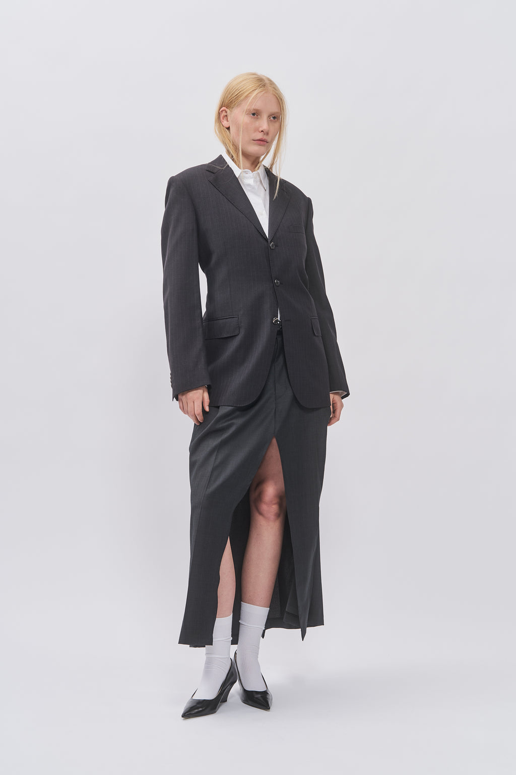 Taus Upcycled Open-Back Blazer in charcoal grey, worn with the matching Upcycled Suit Skirt