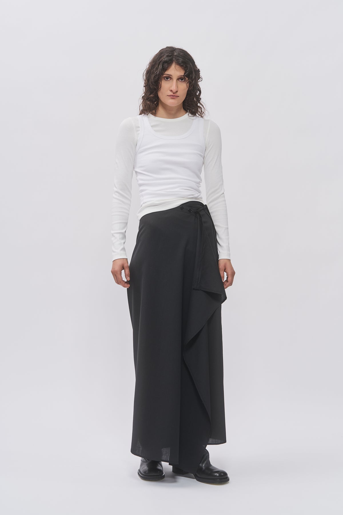 Taus Wrap Skirt in black, maxi skirt with draped front and tie waist, styled with a white long-sleeve top