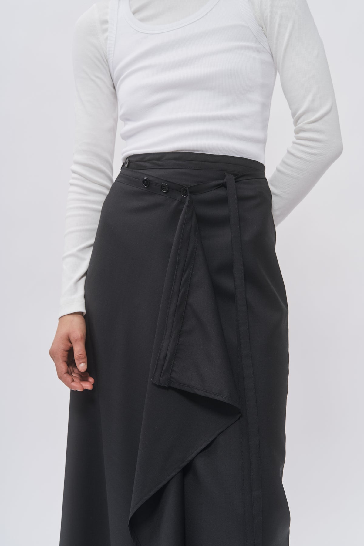 Close-up of Taus Wrap Skirt in black showing the draped wrap panel and tie belt